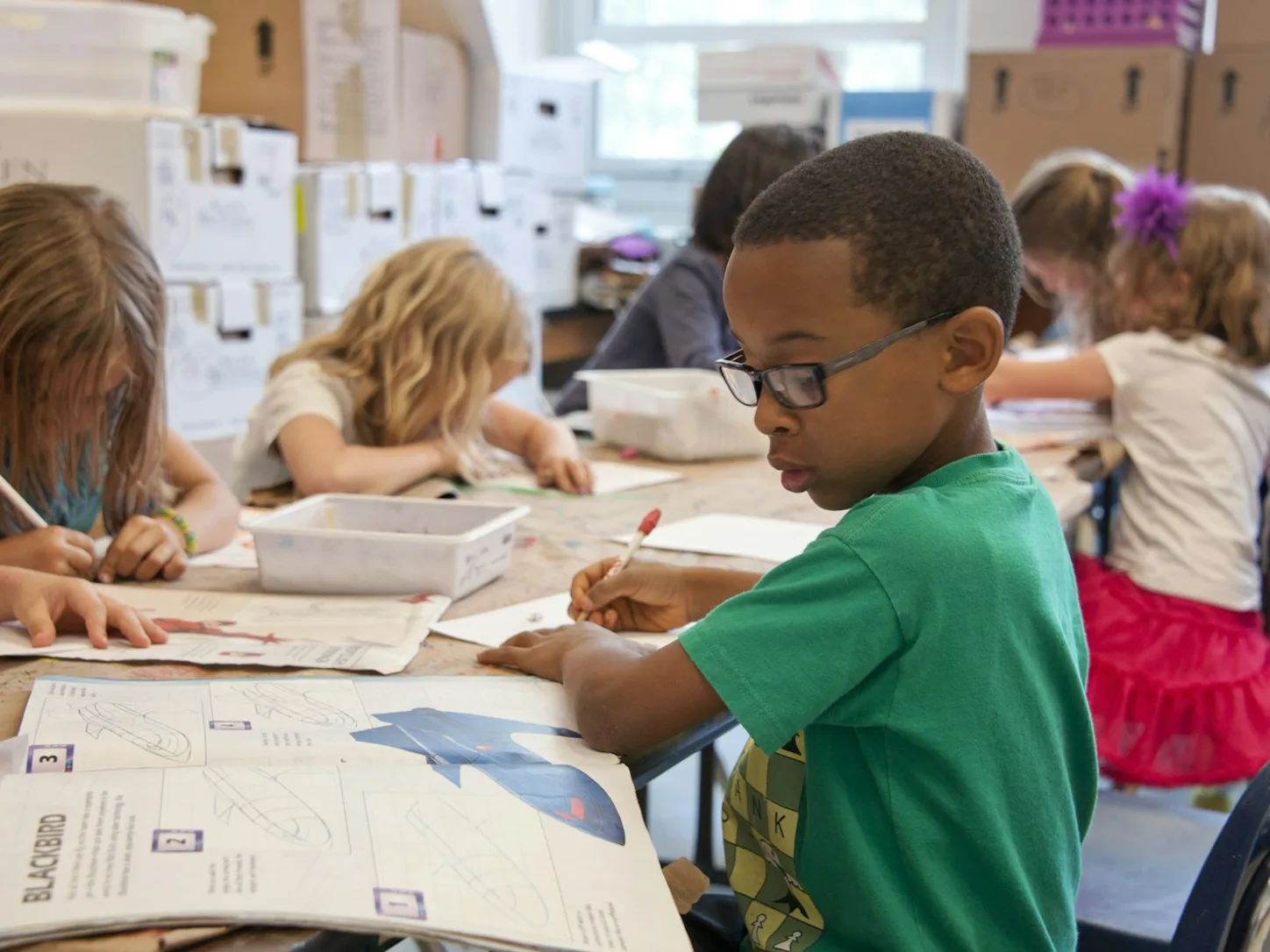 A child drawing at a classroom table during a learning activity